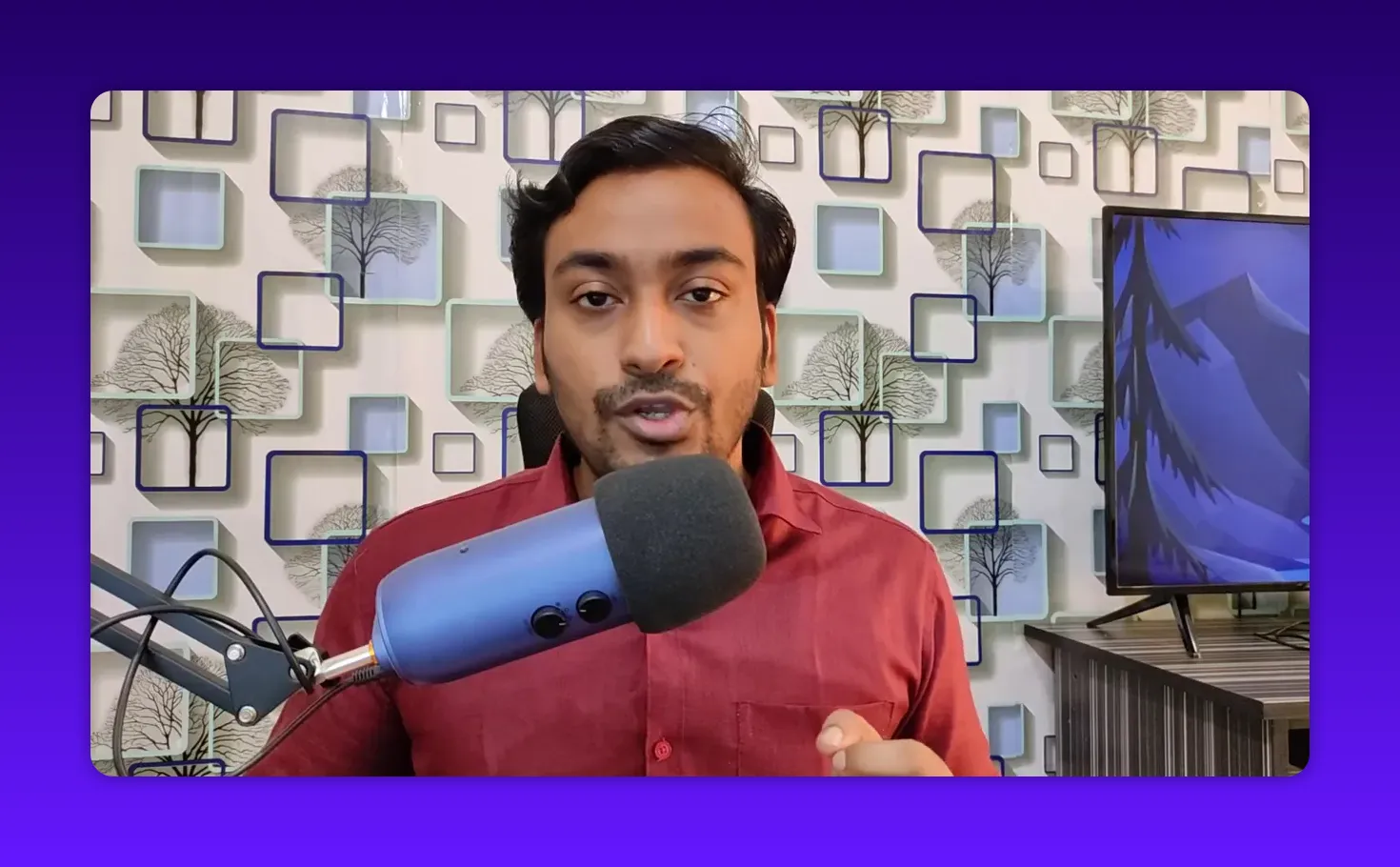 Host speaking into a blue microphone with a patterned wall background and a monitor on the right
